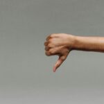 Close-up of a person's hand giving a thumbs down gesture against a gray background.